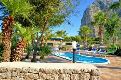 a pool with palm trees and a mountain in the background at Villa Minoa con piscina in San Vito lo Capo