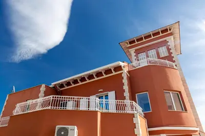a red building with white balconies and a blue sky at Villa Edera Rental Room in Santa Flavia
