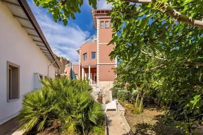 a tall pink building with a building at Villa Edera Rental Room in Santa Flavia