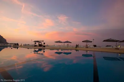 a swimming pool with umbrellas and a sunset in the background at La Marsa Vacances in Mondello