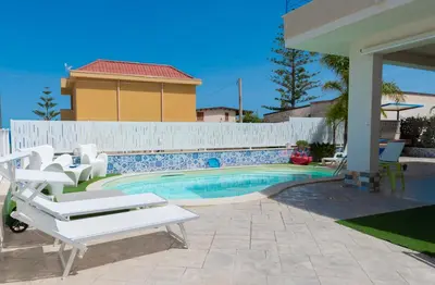 a swimming pool with white chairs and a house at Villa con piscina Alcamo Marina in Alcamo