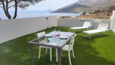 a table and chairs on a patio with a view of the water at Villetta SanVito - Sunrise & Sunset in San Vito lo Capo