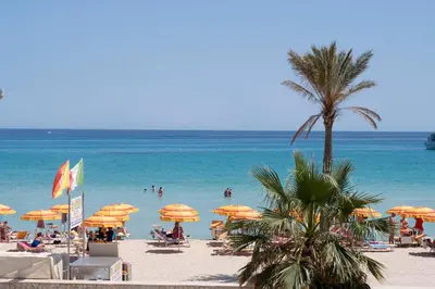 a beach with umbrellas and people in the water at Appartamento Conturrana Sul Mare in San Vito lo Capo