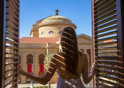 a woman looking out a window at a building at Palazzo Sovrana Serviced Luxury Apartments in Palermo