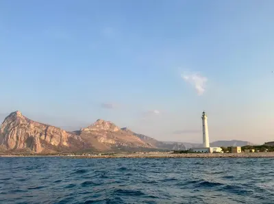 a lighthouse on the shore with mountains in the background at Casa Mandarino in Macari