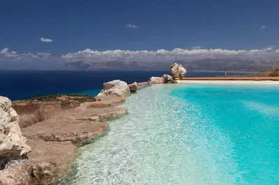a swimming pool with blue water and rocks at Casa Saleiman in Castellammare del Golfo
