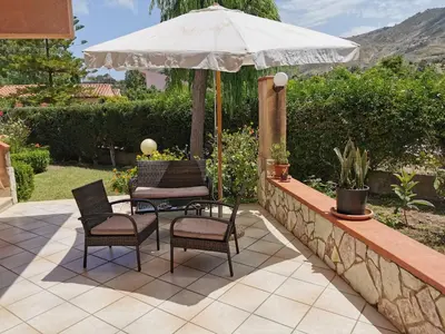 a patio with two chairs and an umbrella at Villetta immersa nel verde ma vicina al mare in Lascari