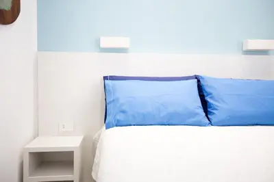 a bed with blue pillows in a white bedroom at White Asses Rooms in Castellammare del Golfo