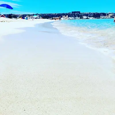a sandy beach with a blue umbrella and the ocean at Krimar Hotel in San Vito lo Capo