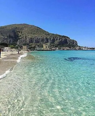 a beach with blue water and a mountain in the background at casa nina in Mondello