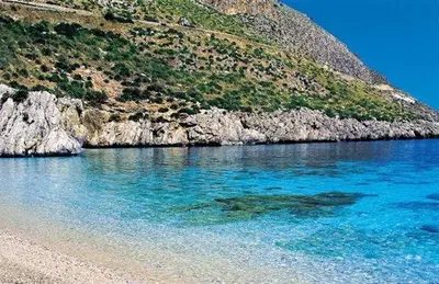 a beach with blue water next to a mountain at Essenzamare in San Vito lo Capo