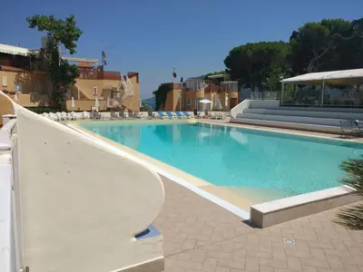 a large blue swimming pool with chairs and buildings at Casa Vacanze Mondello Mare Piscina ALBAMAOR in Mondello