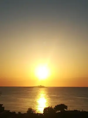 a sunset over the ocean with a small island in the distance at tramonto blu in Palermo