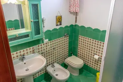 a green and white bathroom with a sink and a toilet at Villa Verde con vista sul mare in San Vito lo Capo