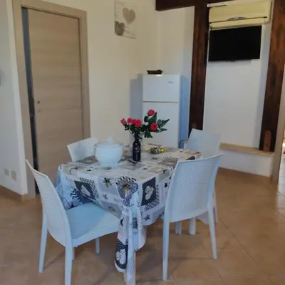 a table with white chairs and a vase of flowers on it at Baglio cracchiolo da tuzzo Villa Ulivo in San Vito lo Capo