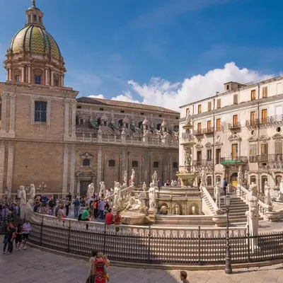a group of people standing around a fountain in front of a building at REALE ORLEANS in Palermo