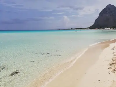 a beach with clear water and a mountain in the background at B&b IL FIOCCO E LA RANDA in San Vito lo Capo
