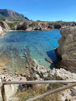 a beach with clear blue water and a wooden fence at La Ruota B&B in Terrasini