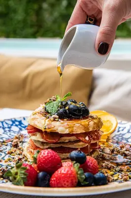 a person pouring syrup onto a stack of pancakes with berries at Casa Nostra Boutique Hotel & Spa in Palermo
