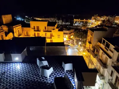 a view of a city at night with two white chairs at Palazzo del Golfo Penthouse in Castellammare del Golfo