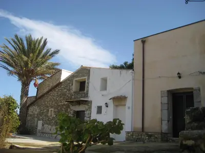 a white building with a palm tree next to it at Il Volo Dei Gabbiani in Scopello