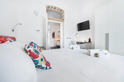 a white bedroom with a bed and a tv on the wall at White in Palermo