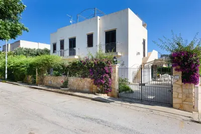 a white house with a fence and purple flowers at Casa Vacanza Azzurra in San Vito lo Capo