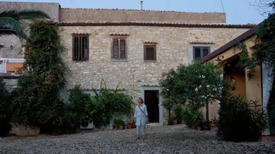 a woman standing in front of a stone building at Agriturismo Ridocco in Corleone