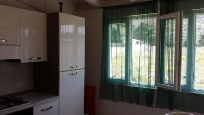 a kitchen with two windows with green curtains at Casa Vacanze Mari in San Vito lo Capo
