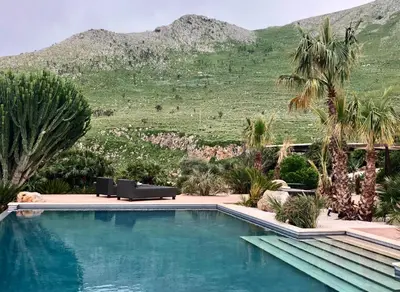 a swimming pool with palm trees and mountains in the background at Baglio La Porta by Geocharme in San Vito lo Capo