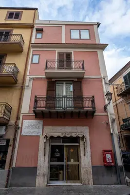 a tall pink building with a balcony on a street at Casa Novelli Apartments in Monreale
