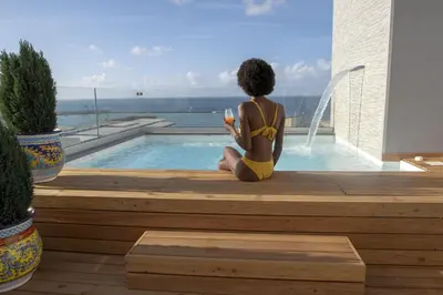 a woman in a yellow bikini sitting next to a swimming pool at Luxmarì Hotel & Spa in Castellammare del Golfo