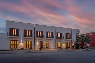 a large white building with a sunset in the background at Hotel Sabbia d'Oro in San Vito lo Capo
