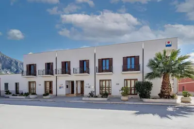 a large white building with a palm tree in front of it at Hotel Sabbia d'Oro in San Vito lo Capo