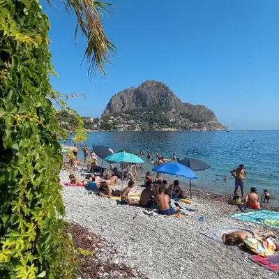 a group of people sitting on a beach with umbrellas at Casa nel borgo marinaro di Santa Nicolicchia in Santa Flavia