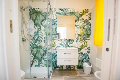 a bathroom with a glass shower with palm trees wallpaper at L' Arcobaleno B&B in Castelluzzo