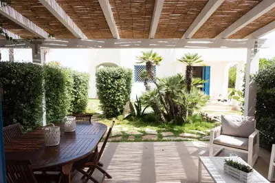 an outdoor patio with a wooden table and chairs at Villa Blumarine sul mare in San Vito lo Capo