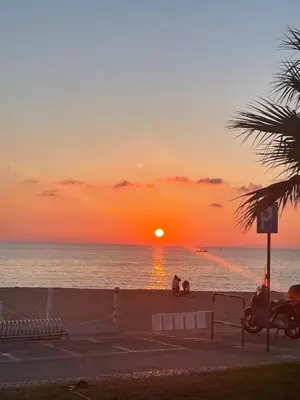 a sunset on the beach with people sitting on the beach at Rosalia Homestay - Ponente Apartment in Cinisi