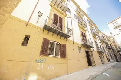 a yellow building with shuttered windows on a street at Casa Raffadali, in centro storico a Palermo in Palermo