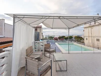 a patio with a white umbrella and chairs and a pool at Apartment in Alcamo near the Beach in Alcamo Marina