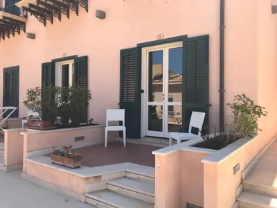 a patio with two chairs and a door and windows at Castellammare Smart Rooms in Castellammare del Golfo