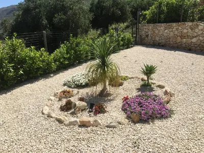 a garden with plants and flowers on a gravel ground at Villa Edori - Giardino degli Allori in Castellammare del Golfo