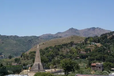 a monument on a hill with mountains in the background at Gibilrossa BeeHill in Misilmeri