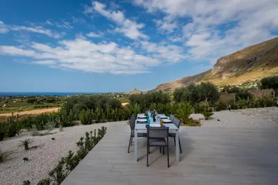 a table and chairs on a patio with mountains in the background at Giardino degli Allori - Villa Flores in Castellammare del Golfo