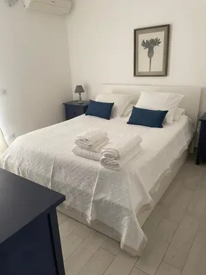 a white bed with white sheets and blue pillows at Villa Costanza in San Vito lo Capo
