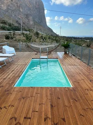 a swimming pool on a wooden deck with a mountain in the background at Villa Costanza in San Vito lo Capo