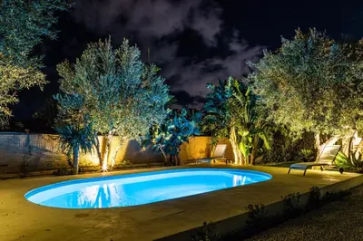 a swimming pool in a yard with trees at night at Villa Bienvenue in Carini