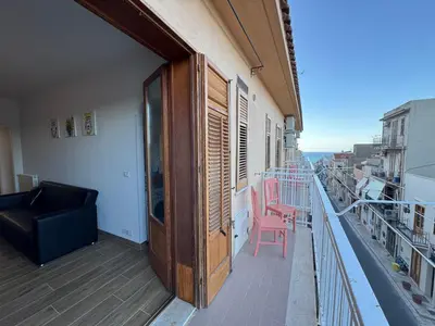 a balcony with a black couch and a pink chair at Made In Sicilia -IN CENTRO, ARIA CONDIZIONATA e NO ZTL- CITY CENTRE, AIRCON and NO LTZ in Castellammare del Golfo