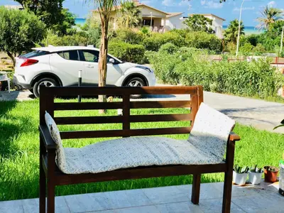 a bench sitting in the grass with a car in the background at VILLA OASI a 50 mt dalla spiaggia in Alcamo Marina