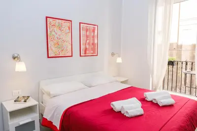 a white bedroom with a red bed with two towels on it at Appartamenti Maria Al Capo in Palermo